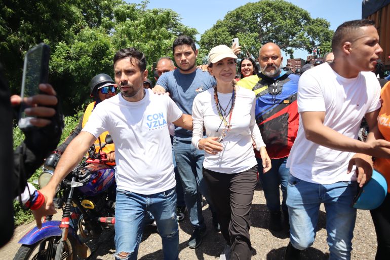 Maria Corina Machado is escorted through a blockade on the road to Maracaibo, a man parting the crowds with a hand on her back.