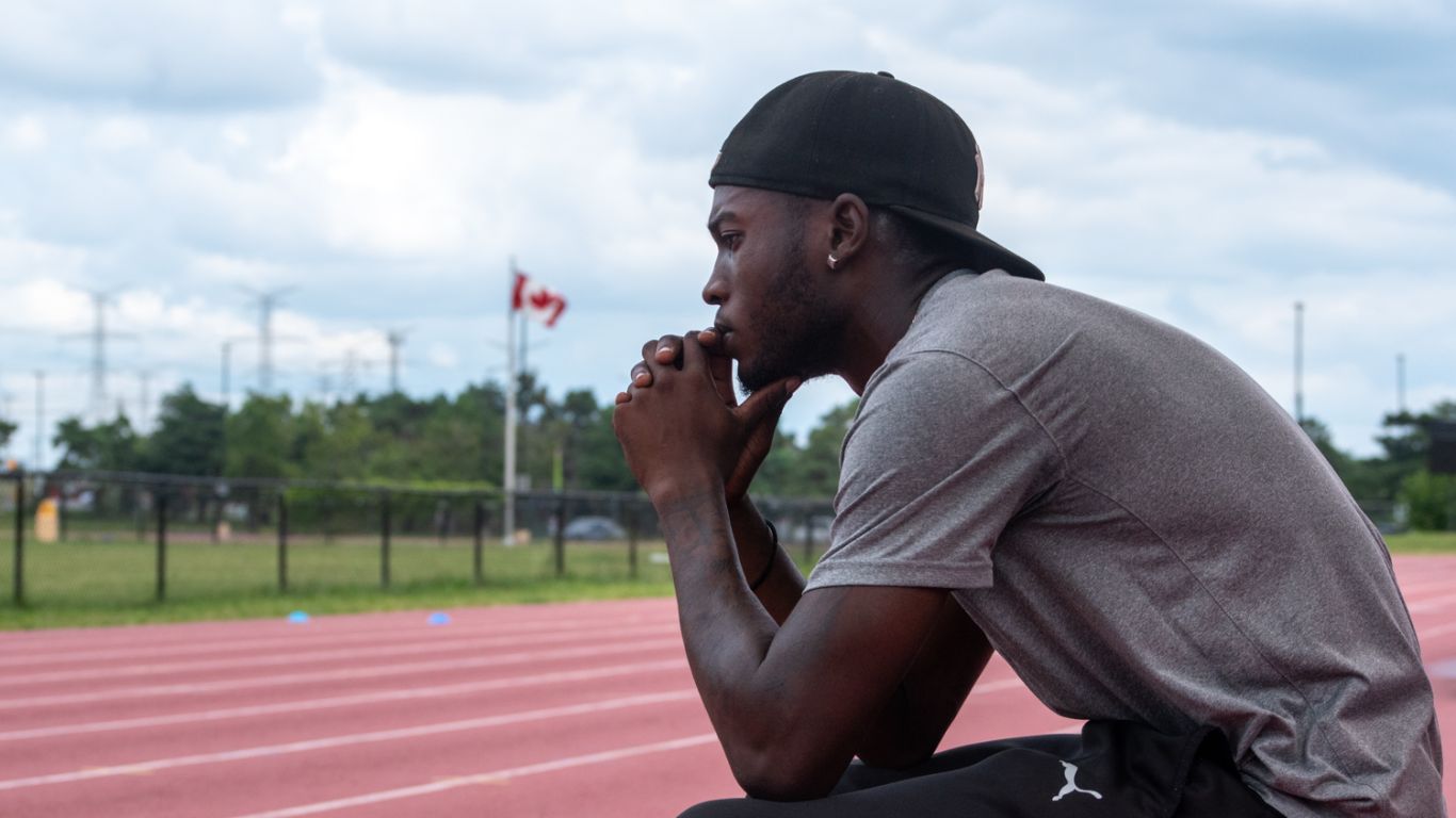 Tamarri Lindo sits on a bench, looking out over an outdoor track.