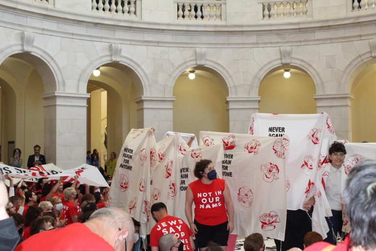 Protesters lift white sheets on the floor of the Cannon building, with slogans reading: "Never again for anyone."