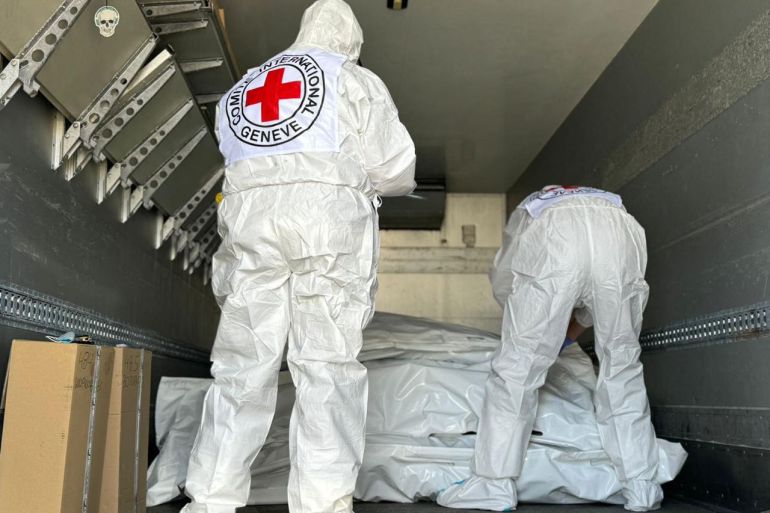 ICRC representatives check body bags in the exchange between Russia and Ukraine. They are wearing white hazmat suits with the Red Cross logo on the back. The body bags are also white.