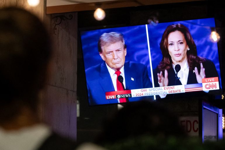 A walking past stops to watch a screen displaying the US Presidential debate between Vice President and Democratic presidential candidate Kamala Harris and former US President and Republican presidential candidate Donald Trump