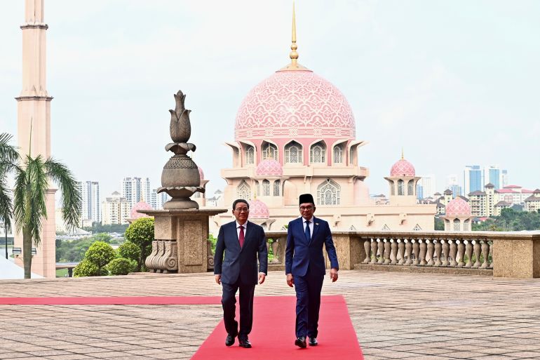 Anwar Ibrahim and Li Qiang walking along a red carpet. There is a mosque with a pink dome behind them.