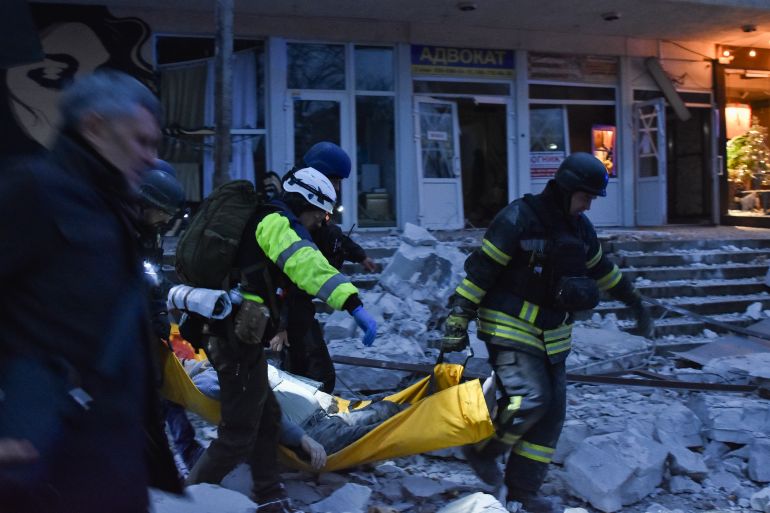 people carry a body near a destroyed dbuilding