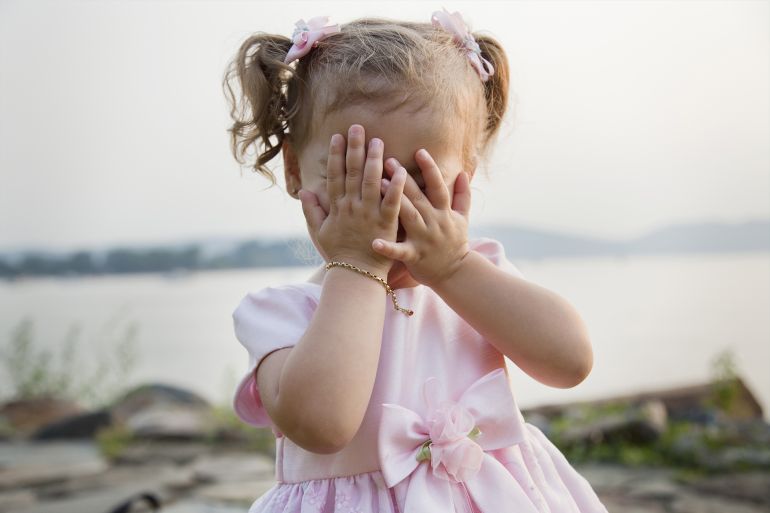 Young girl in party dress cover face as if playing peek-a-boo, or as if hiding غيتي