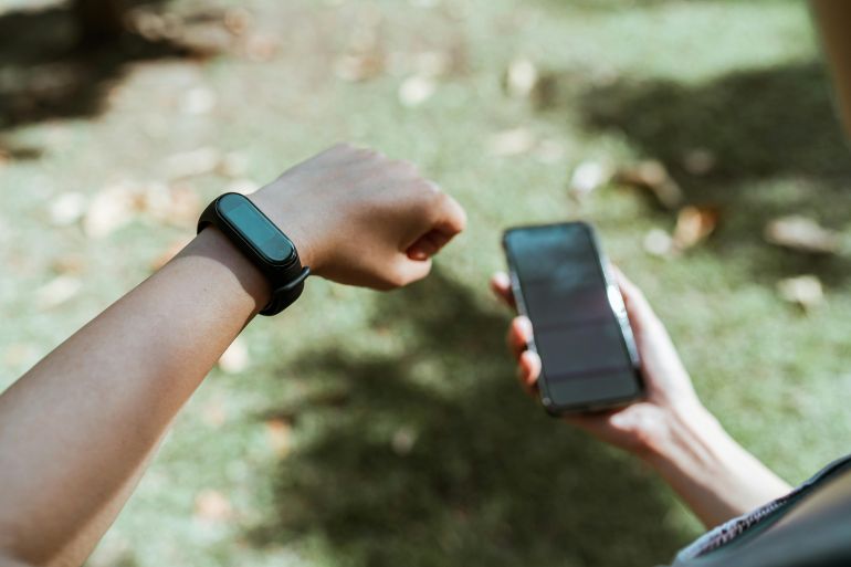 Crop faceless person showing smart watch while using smartphone outdoors