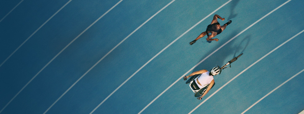 Deux athlètes font la course sur une piste. L’une court et l’autre utilise un fauteuil roulant de course.