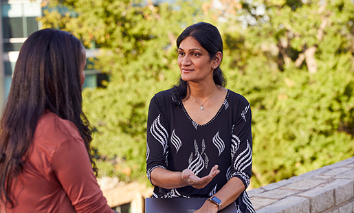 Ramani pratar med en arbetskamrat på en plats med träd utomhus.