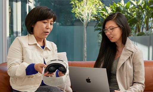 Jessica usa una MacBook en el interior con una puerta abierta hacia un patio, está sentada con otra colega de Apple que sostiene el Apple Vision Pro.