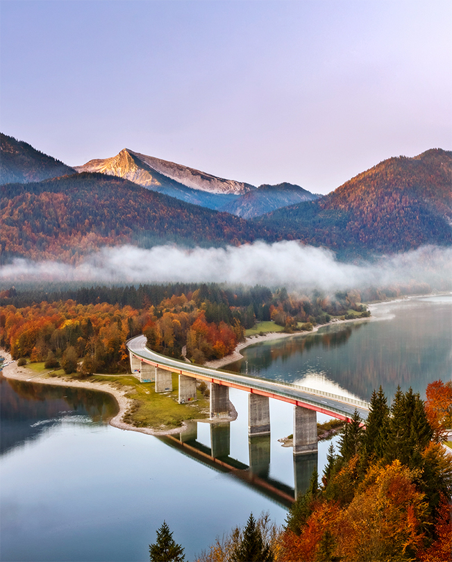 Eine Brücke, die über einen See führt, mit Bergen im Hintergrund.