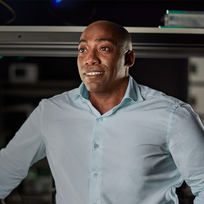 Mike smiling and looking off to the left in an engineering facility, surrounded by equipment.