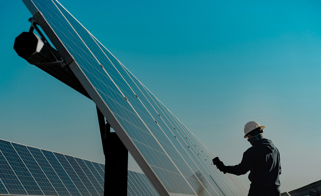 Un hombre con casco trabajando en un gran panel solar en el exterior.