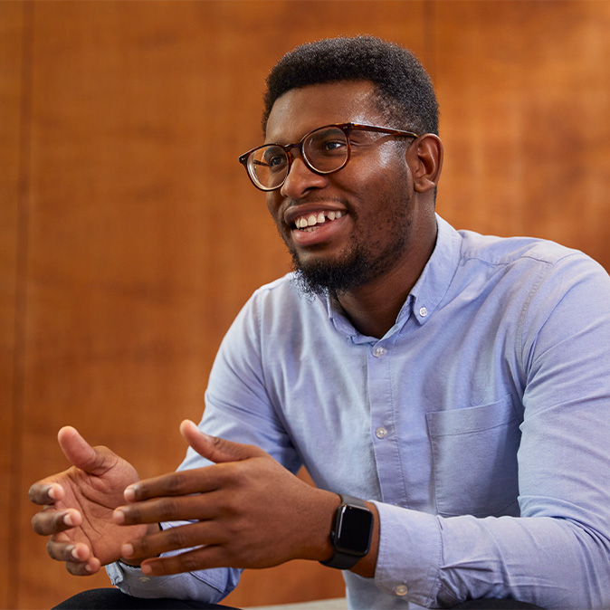 Chidi, souriant, est assis le regard tourné vers le côté.