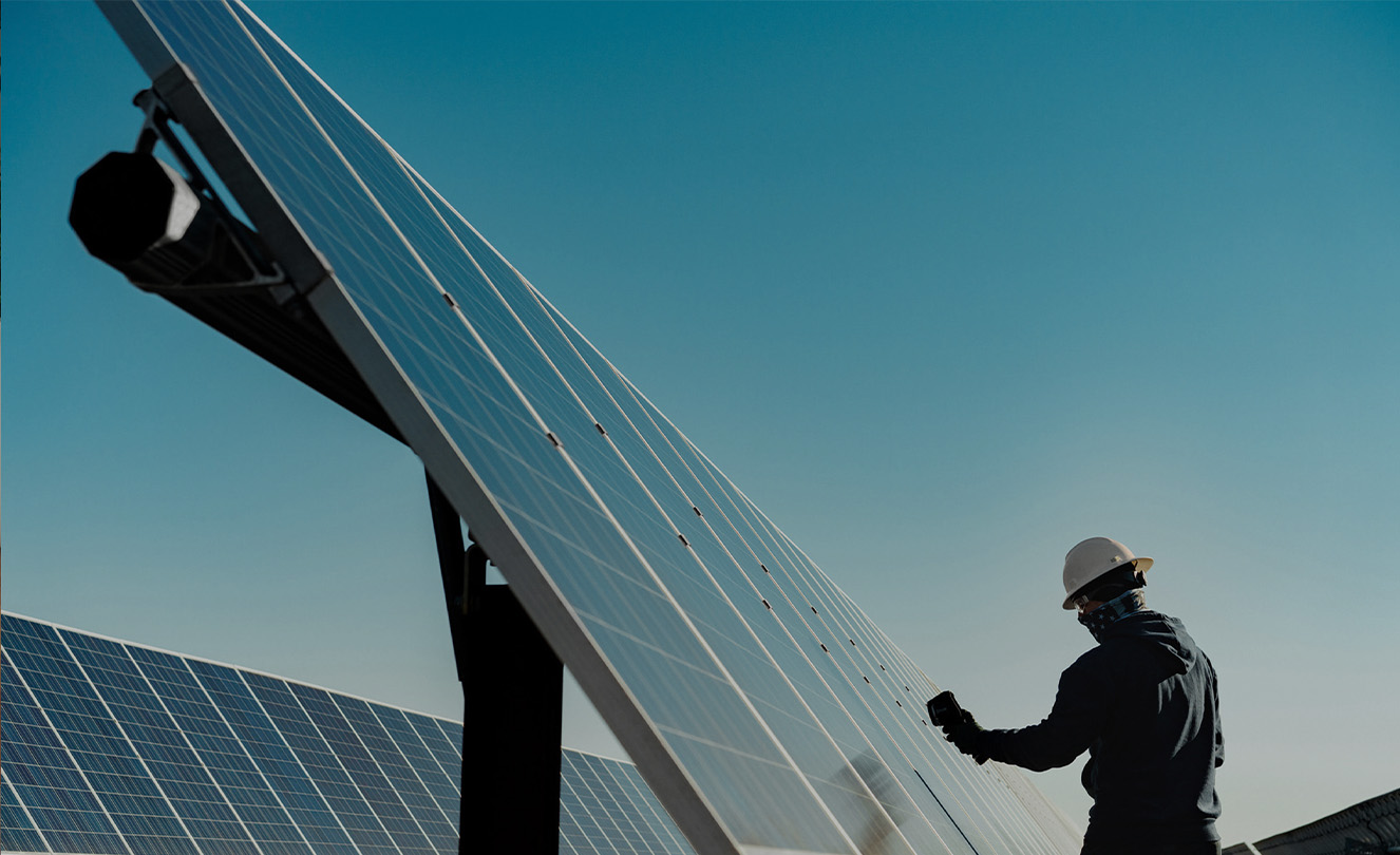 Un homme portant un casque de protection travaille sur un grand panneau solaire à l’extérieur.