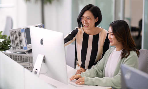 Ella de pie junto a otra persona del equipo que está sentada frente a una pantalla de Apple.