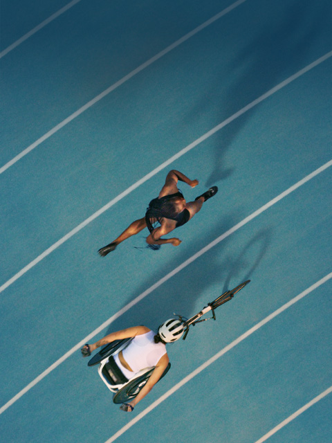 Two athletes racing each other on a track, one is running and the other is in a racing wheelchair.