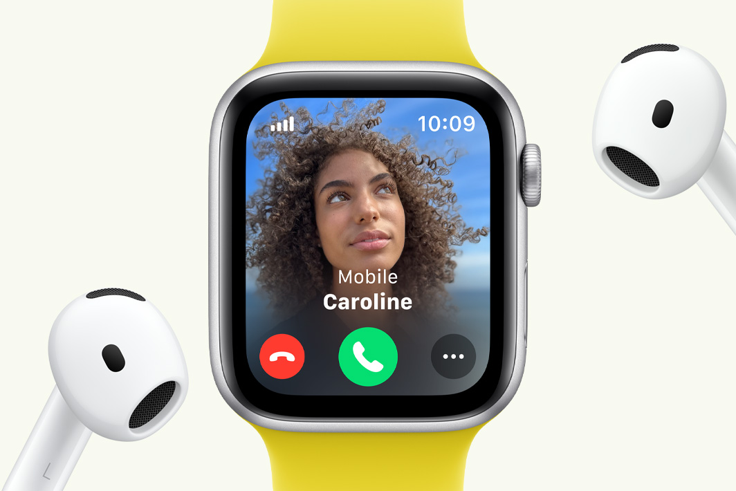 Apple Watch SE, na którym widać połączenie przychodzące, ustawiony obok pary słuchawek AirPods