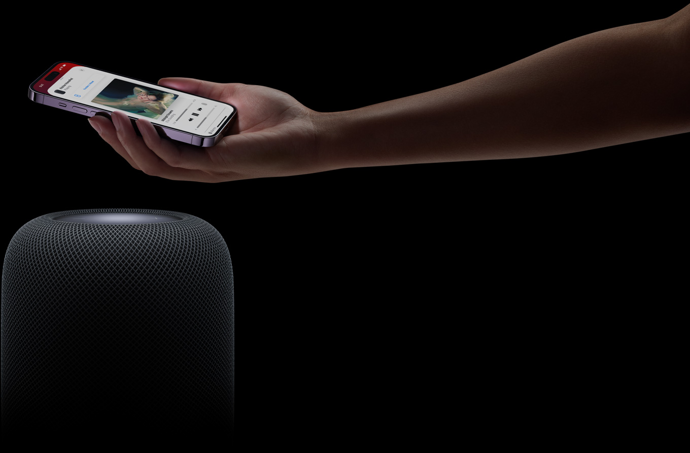 Eine Hand, die von rechts kommt, hält ein iPhone über einen HomePod Lautsprecher