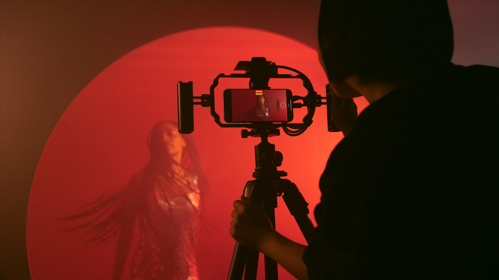 A photo of someone using an iPhone on a tripod to record a colorful video of a woman