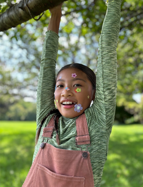 Fotografia de grande plano de uma mulher com stickers de flores no rosto tirada com a Teleobjetiva com zoom ótico a 2x no iPhone 15