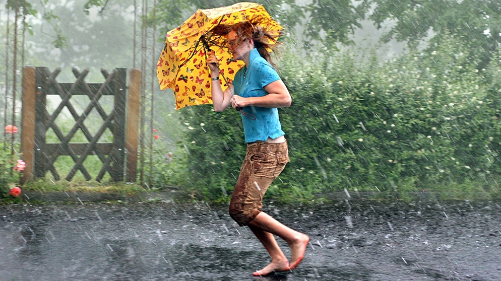 Frau mit Schirm läuft durch den Regen. - Vorsicht mit metallhaltigen Gegenständen bei Gewitter: Sie leiten Strom und können euch ernsthaft gefährden. | Bild: picture-alliance/dpa