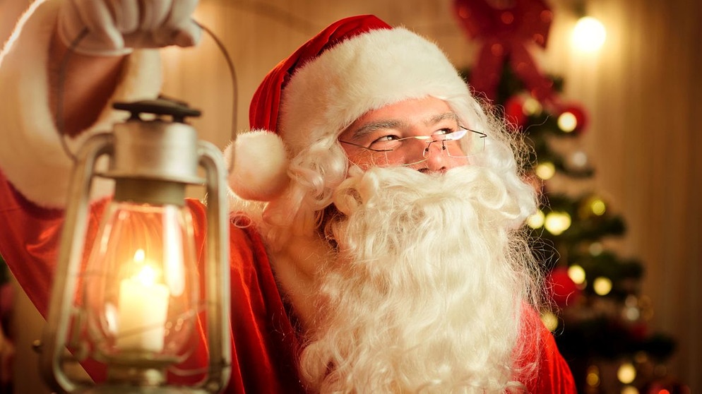 Nikolaus vor einem Christbaum hält eine Lampe in der Hand. Hier erfahrt ihr spannende und kuriose Fakten über Weihnachten: Welches ist der beliebteste Weihnachtsbaum, wo stand der größte Christbaum der Welt - und was ist eine Weihnachtsgurke?  | Bild: colourbox.com