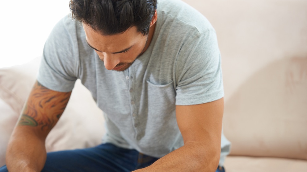 Mann sitzt gebäugt auf einem Sofa. Grübeln wir, bewegen sich unsere Gedanken wie in einem Gedankenkarussell. Wir erklären euch die Ursachen für euren Grübelzwang und wie ihr negative Gedanken stoppen könnt. | Bild: colourbox.com