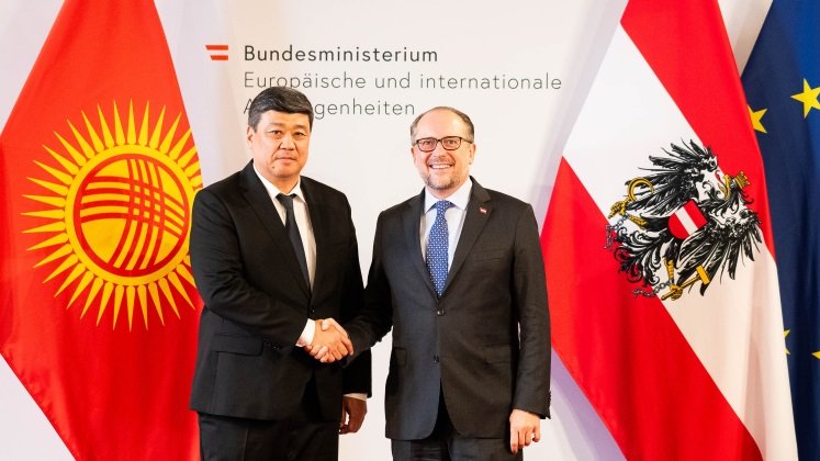 Außenminister Schallenberg steht neben dem stellvertretenden Premierminister Kirgisistans, Bakyt Torobaev. Sie schütteln einander die Hände und blicken lächelnd in die Kamera. Im Hintergrund sind die österreichische, die EU sowie die kirgisische Flagge aufgestellt.