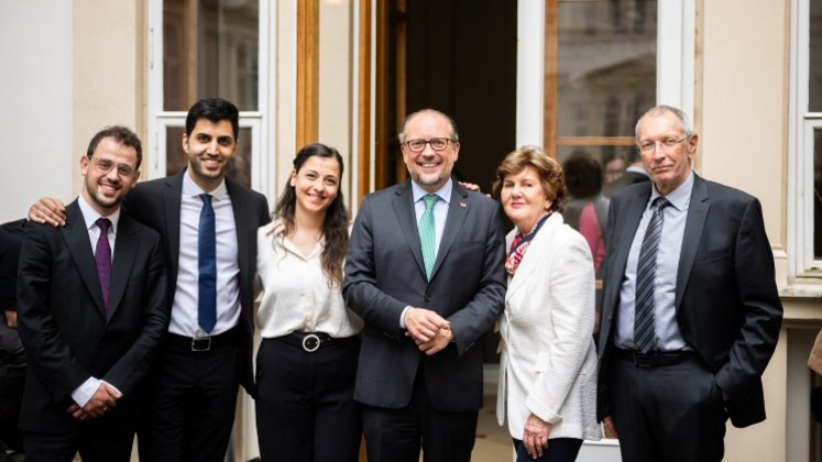 Außenminister Alexander Schallenberg steht zusammen mit den Musikerinnen und Musikern des „West Eastern Diwan Orchestra“ sowie mit Helga Rabl-Stadler und Philosoph Konrad Paul Liessmann. Sie blicken lächelnd in die Kamera. 