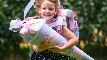 Die kleine Lina aus Sachsen rennt nach der Schuleingangsfeier mit ihrer Zuckertüte in den Armen über einer Wiese in der Nähe der Grundschule.  | Bild: dpa-Bildfunk/Robert Michael