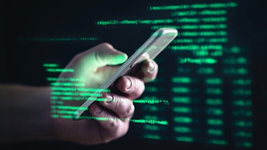 Eine Männerhand mit einem Smartphone in dunkler Umgebung mit leuchtend grünen Computercodes. | Bild: stock.adobe.com/terovesalainen