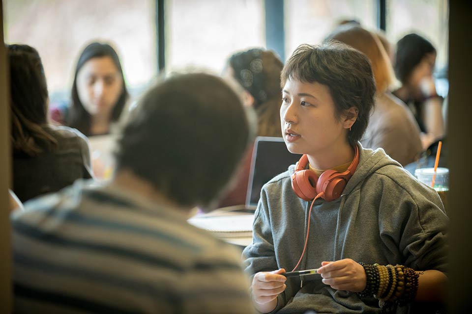 Student with headphones around neck talking with others in a class