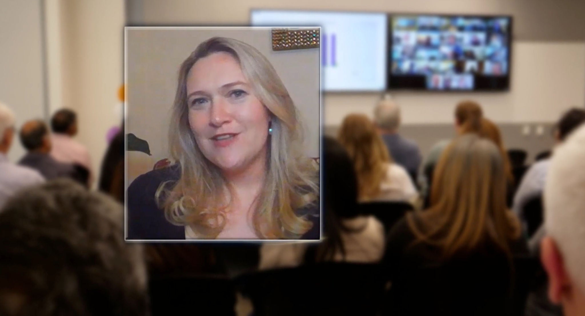 employee smiling with employees meeting in background