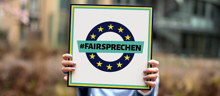 Hände halten Schild mit "Fairsprechen"-Logo