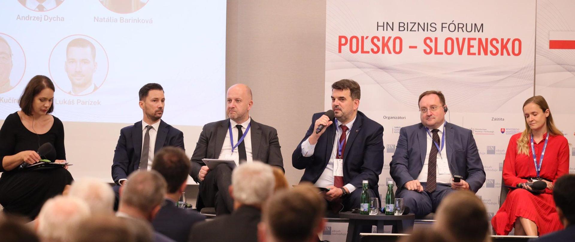 Wiceminister Jacek Tomczak na polsko-słowackim Forum Biznesu. Na zdjęciu widać panelistów Forum. Wiceminister zabiera głos, obok niego siedzą inni uczestnicy debaty, przed którymi siedzi publiczność.