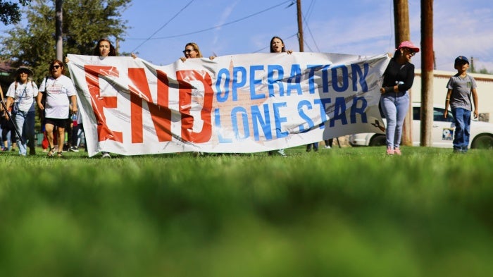 People hold a banner during a protest against Operation Lone Star after members of the Texas National Guard shot and wounded a 22-year-old near the Bridge of the Americas in El Paso, Texas, September 1, 2023. © 2023 REUTERS/Jose Luis Gonzalez