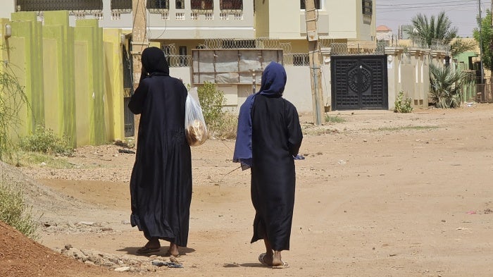 Two unidentifiable women walk down a city street 