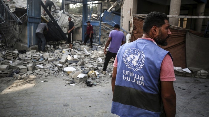 Workers stand in front of the ruins of a school building