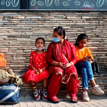 A woman and two young girls sit at a bus station