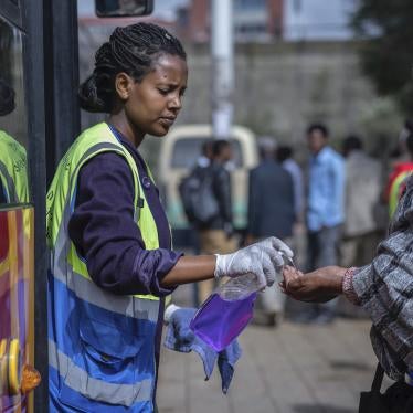 A volunteer provides hand sanitizer to passengers entering a bus