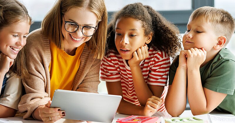 Grundschullehrerin zeigt drei Schülerinnen und Schülern ein animiniertes Bilderbuchkino auf einem Tablet.