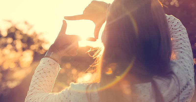 Mädchen macht mit vier Fingern ein Rechteck vor dem Sonnenuntergang