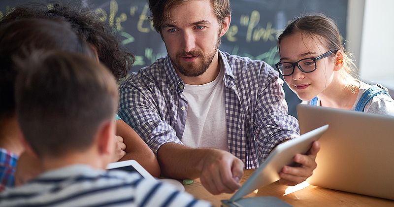 Lehrer mit iPad mit seinen Schülerinnen und Schülern im Unterricht.