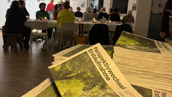 Blick auf eine aktuellen Zeitung und in die neu eröffnete Ausstellung "Perspektivwechsel Erstaufnahme" im Community Art Center in Suhl.