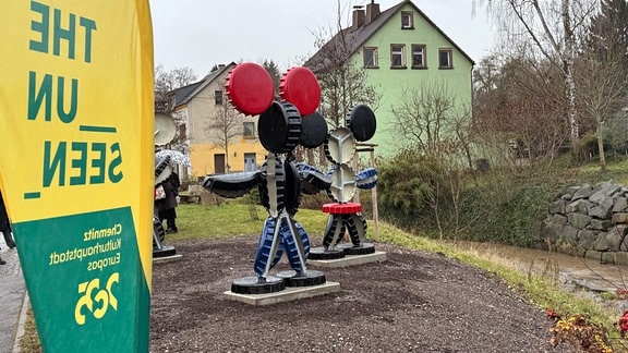 Blick auf Skulpturen vor zwei Häusern: Mehrere farbige Scheiben in Form der Comic-Figur Mickey Maus.