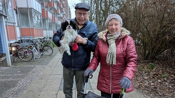 Ursula Jostock und Helmut Brunlieb stehen mit einem Hund vor dem Wohnblock "Lange Lene" und schauen in die Kamera. 