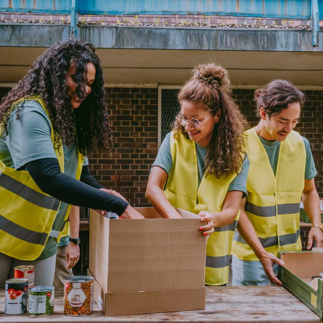 Three Volunteers in blue shirts and yellow vests sorting canned goods in boxes