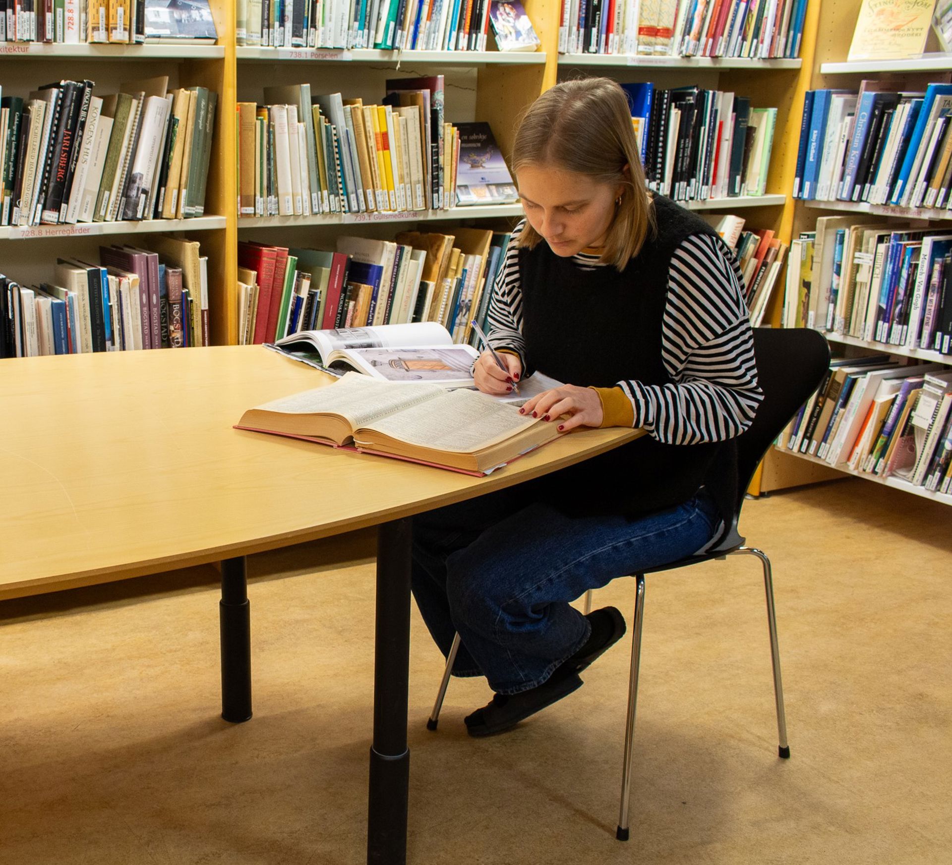 Ung kvinne blar i bøker på biblioteket.