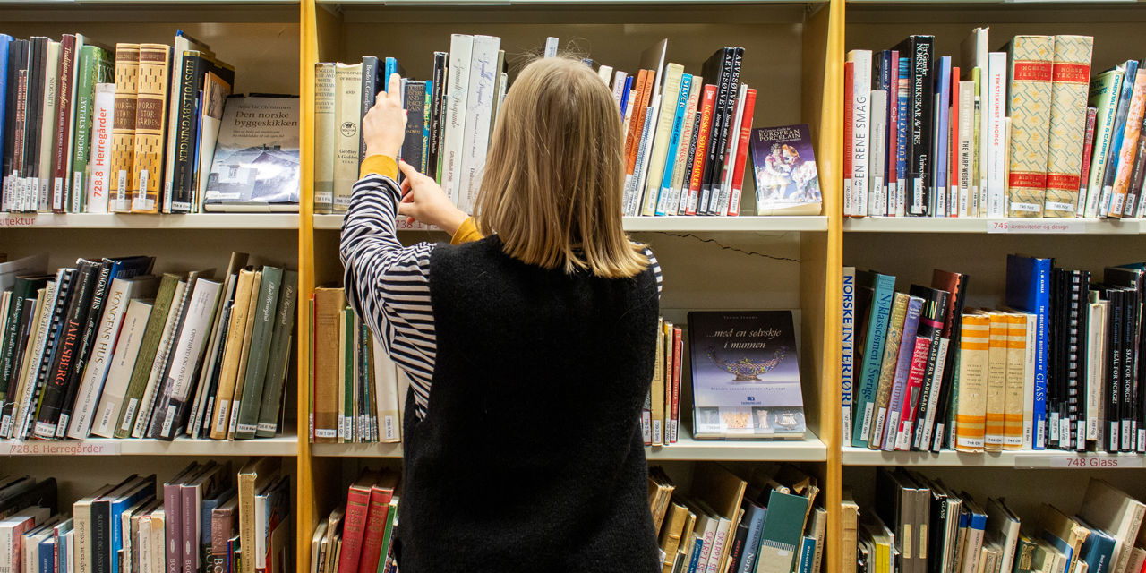 Ung kvinne ser i hyllene på  biblioteket