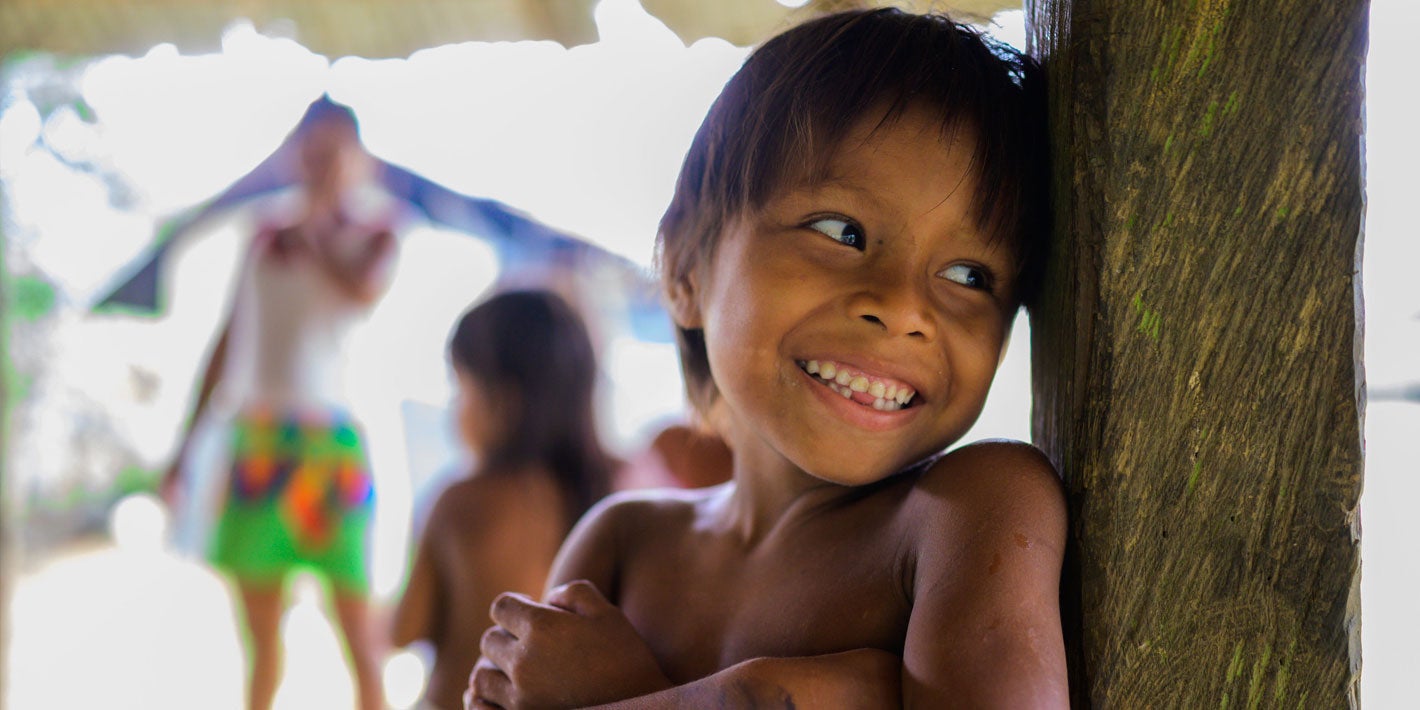 Niño sin camisa recostado contra una pared y sonriendo