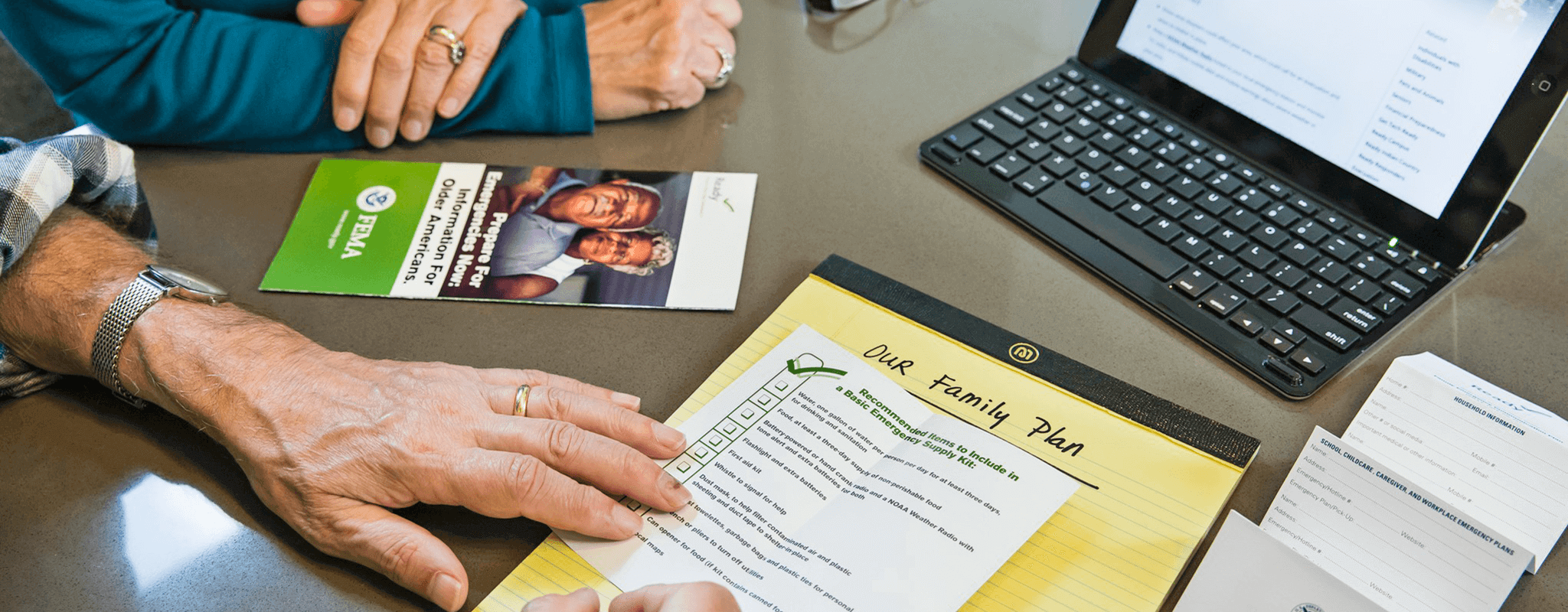 Hands of older couple making a list of disaster preparation actions in front of a laptop